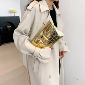 Golden crocodile embossed envelope clutch bag with metal buckle held by woman in coat