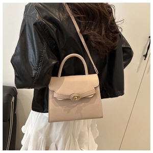 Detail of a beige trapezoid crossbody bag with wavy flap design and gold twist lock