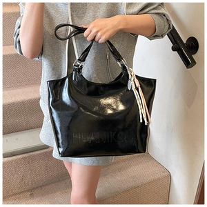 Detail of black glossy tote bag featuring brand embossing and colorful rope tassel charm