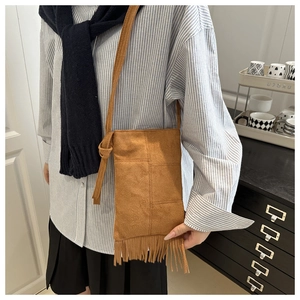 Detailed view of brown suede crossbody bag featuring long bohemian tassels and knots