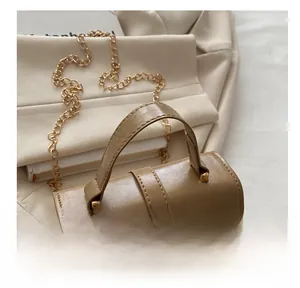 Detail of light brown leather mini bag with gold chain strap on soft white fabric