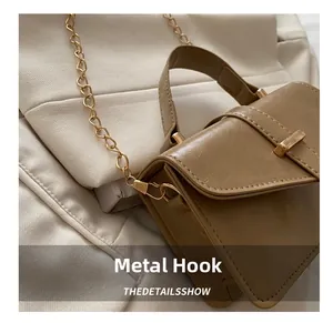 Close-up of golden metal hook hardware on brown textured leather crossbody bag