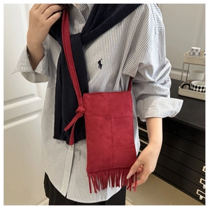 Fashionable red suede crossbody bag with bohemian fringes worn over a striped shirt