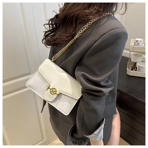 Detail of white leather shoulder bag featuring gold M-logo buckle and floral embossing