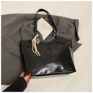Detail of glossy black tote bag featuring embossed logo and braided rope pendant accessory