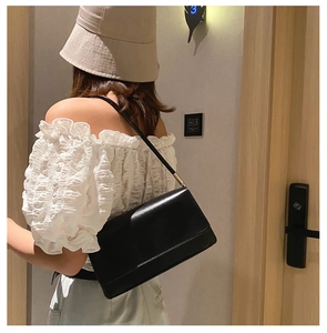 Minimalist black leather underarm bag with rectangular flap shown on shoulder