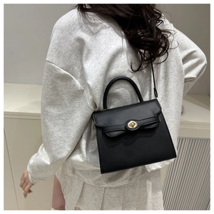 Detail of black crossbody bag with gold twist lock on model in minimalist setting