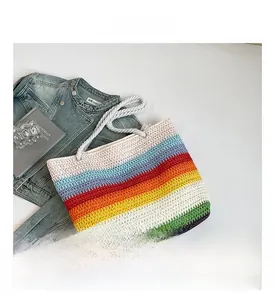 Détail du sac en paille tressé à rayures arc-en-ciel sur fond blanc avec veste en jean
