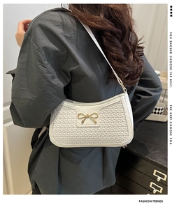 Détail du sac baguette blanc à texture croco avec boucle nœud doré porté à l'épaule