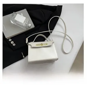 Close-up of cream square handbag with gold lock and phone for size reference