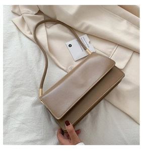 Detail of taupe minimalist leather shoulder bag with gold hardware on beige blazer