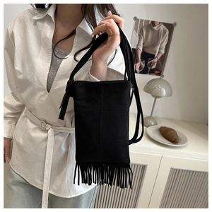 Detail of a black suede crossbody bag featuring retro tassels and a minimalist design