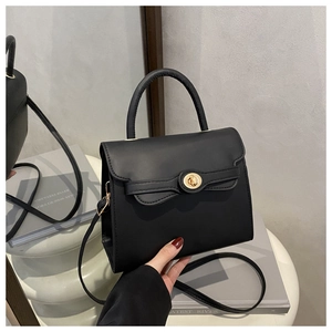 Detail view of black matte leather handbag with gold circular lock and shoulder strap