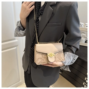 Detail of floral embossed beige baguette bag with golden M buckle and metal chain strap