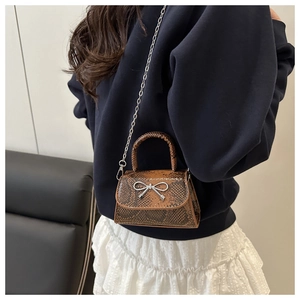 Detail einer braunen Mini-Tasche mit Schlangenmuster, silberner Schleife und Metallkette