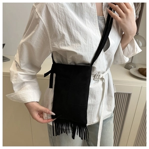 Close-up of black suede crossbody bag featuring bohemian fringe and side knot details