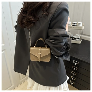 Detail of a mini khaki leather crossbody bag with metal buckle and thin chain strap