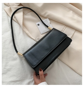 Detail of black faux leather baguette bag showing golden cylindrical metal hardware