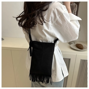 Detail shot of a black suede fringe crossbody bag worn with a white shirt