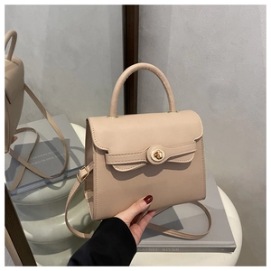 Detail of nude leather satchel with metal twist lock and handle on grey book props