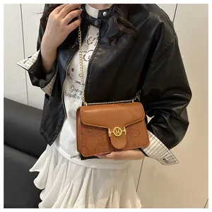 Detail of brown baguette bag featuring gold M-buckle and floral embossed leather pattern