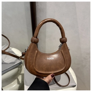 Dettaglio di borsa a mezzaluna marrone con scritta FASHION, manico spesso e nodi decorativi