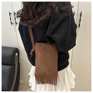 Close-up of brown suede crossbody bag with long fringe tassels and delicate strap detail