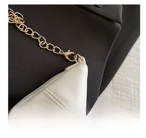 Detailed close-up of golden metal lobster clasp and chain on a white leather bag