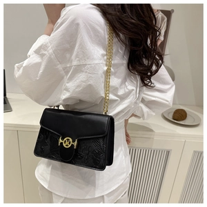 Detail of black embossed baguette bag with gold M buckle and chain on a stylish model