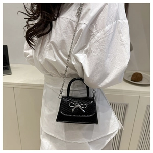 Detail of black snake pattern mini bag featuring a silver metal bow and shiny texture