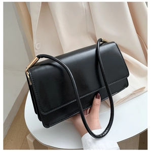 Close-up of black leather shoulder bag featuring elegant gold cylinder hardware accents
