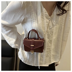 Detail of dark red mini handbag with gold U-shaped buckle and metallic chain strap