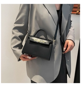 Sac bandoulière minimaliste en cuir noir porté par un mannequin avec un blazer gris