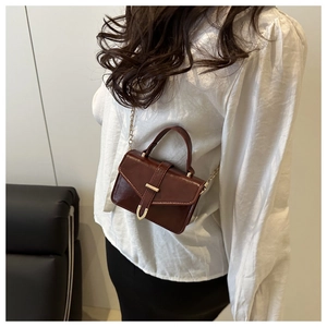 Detail of dark brown mini crossbody bag with gold hardware and shiny leather finish