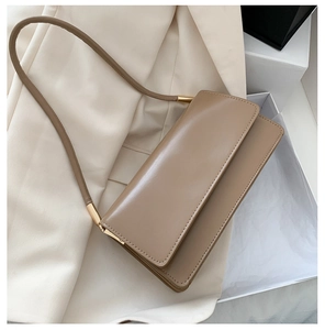 Minimalist khaki leather shoulder bag on white blazer with golden metal hardware detail