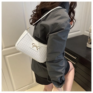 Vue latérale du sac à bandoulière tissé blanc avec boucle nœud dorée porté par un modèle