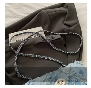 Détail d'un sac bandoulière en denim avec chaîne argentée et fermoir rotatif en métal