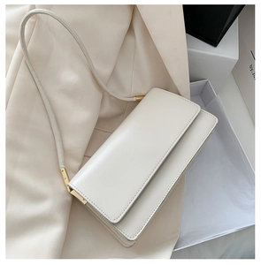 Detail of a creamy white leather shoulder bag with gold hardware and flap closure