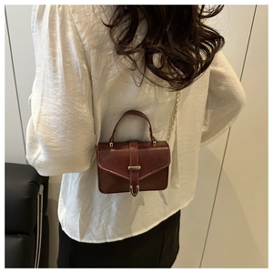 Detail of burgundy leather handbag with gold metal buckle and elegant chain strap