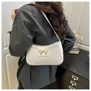 Sac baguette blanc tissé avec nœud doré porté à l'épaule pour un style élégant