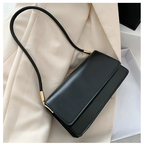Macro view of black leather underarm bag with gold cylindrical metal hardware and smooth finish