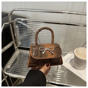 Close-up of a mini dark brown snake pattern crossbody bag with a silver metal bow