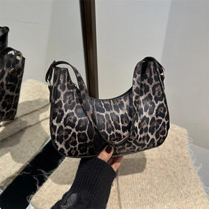 Sac hobo élégant à motif léopard avec boucle dorée tenu sur un fond de ton chaud