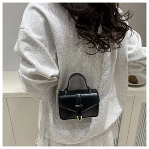 Detail view of a black leather crossbody bag with gold chain strap on a model