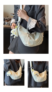 Detail of light beige crescent nylon crossbody bag with textured pleats and plush pendant