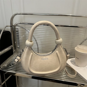 Borsa a mezzaluna beige minimalista con manico rotondo e tracolla su uno scaffale