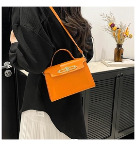 Detail view of orange leather handbag with metal buckle and shoulder strap on model
