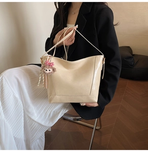 Chic cream leather bucket tote with plush bear charm accessory and shoulder strap