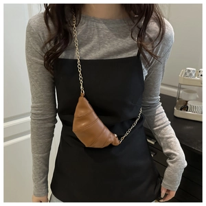 Detail of a brown leather croissant bag with pleated texture and golden chain strap