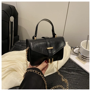 Detail of black glossy faux leather handbag with golden horseshoe buckle and chain strap
